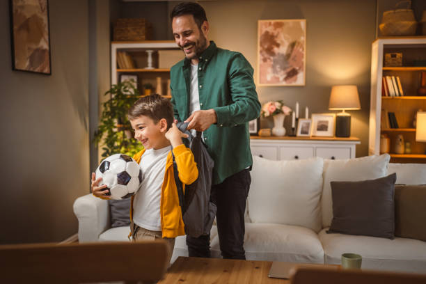 istock Dad help his son who hold football ball to pack for school in backpack 2155648552