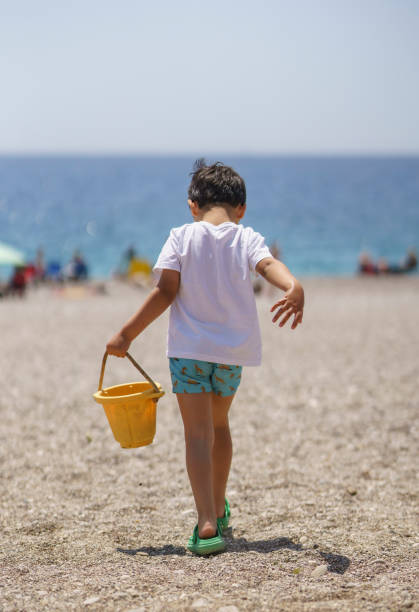 Hispanic elementary age boy and his adult sister collect seashells during beach vacation.