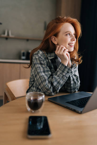istock Vertical portrait of happy young woman using laptop computer at kitchen table, working from home office, smiling looking away, thinking over successful idea 2155657536