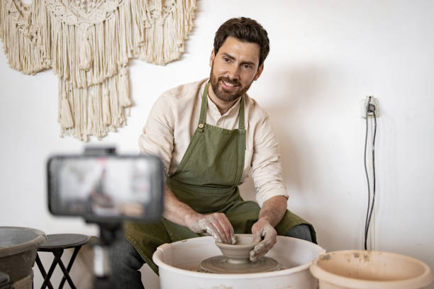 istock Male potter sculpting ceramic vase while recording video blog 2155657876