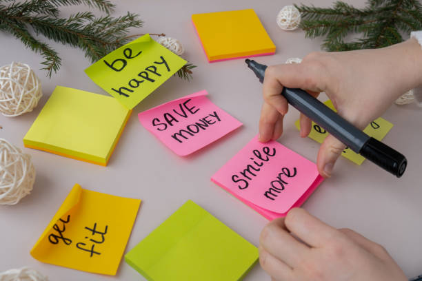 istock Unrecognizable woman writing new year's resolutions on colorful sticky notes. Making promises for new year, setting goals. Creating vision board 2155668388