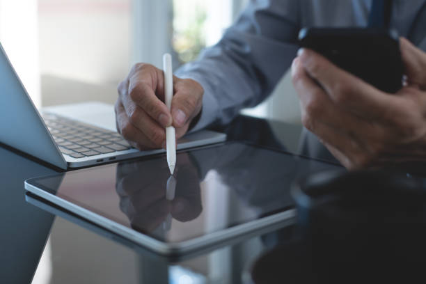 istock Businessman, manager using stylus pen signing e-document on digital tablet with laptop computer on table at modern office, e-signing, electronic signature, paperless office, digital document concept 2155669473