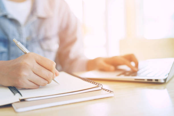 istock close up hand young man are sitting using pen writing Record Lecture note pad into the book on the table wood. 2155672912