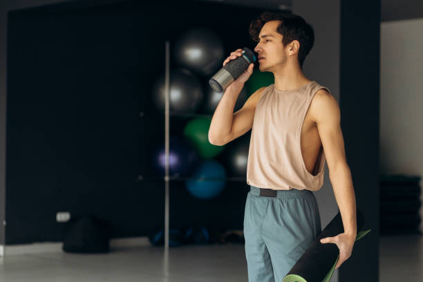 istock Yoga man drinks water from bottle. Handsome young man hold karimat in hand 2155684841