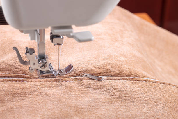 Modern sewing machine special presser foot with beige fabric and thread, closeup. Sewing process of sewing on a zipper. Business, hobby, handmade, zero waste, recycling, repair concept.