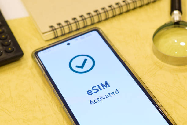 istock Mobile phone displaying the message eSIM activated. Digital SIM or embedded SIM to allow cellular connection, desk with office supplies, close up image. 2155697692