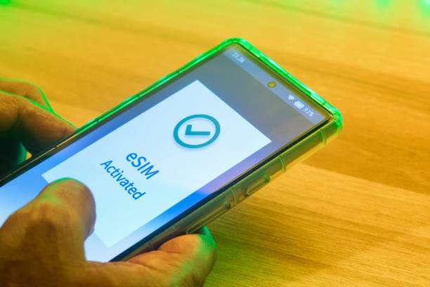 istock Man holding a Mobile phone displaying the message eSIM activated. Digital SIM or embedded SIM to allow cellular connection, travel purpose, close up image. 2155697698