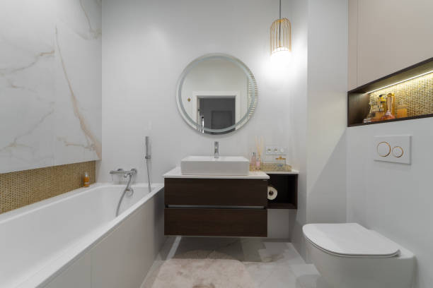A stylish bathroom featuring a sleek bathtub, modern vanity with round mirror, and elegant lighting. The design incorporates warm tones and high-end finishes for a luxurious feel.