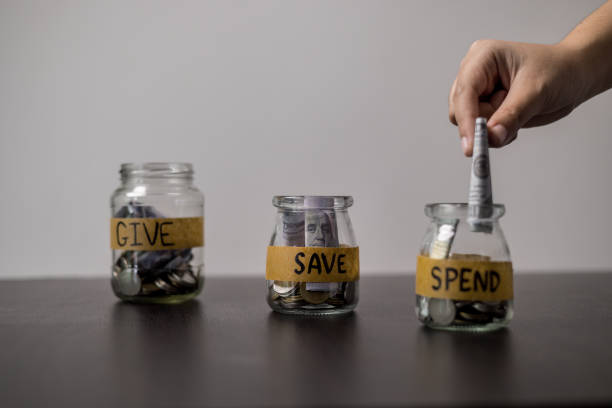 istock Give, Save, Spend money jars. She organized her finances into three jars labeled Give, Save and Spend, ensuring a balanced approach to managing her money. words, lettering, donate, jar, money. 2155702945