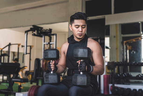 istock An asian man mentally preparing himself while sitting on an incline bench holding two dumbbells placed on his thighs near the knees preparing to do a set of seated dumbbell shoulder presses. 2155703070