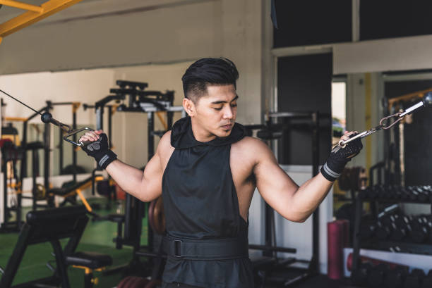 istock A serious asian man in his 20s does standing overhead bicep cable curls. Wearing a black low cut tank top. Training arms at the gym. 2155703509