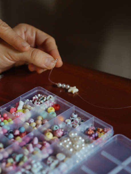 istock Kid Craft with Beads: A vertical close-up shot captures a woman’s hands creating bead jewelry. 2155710175