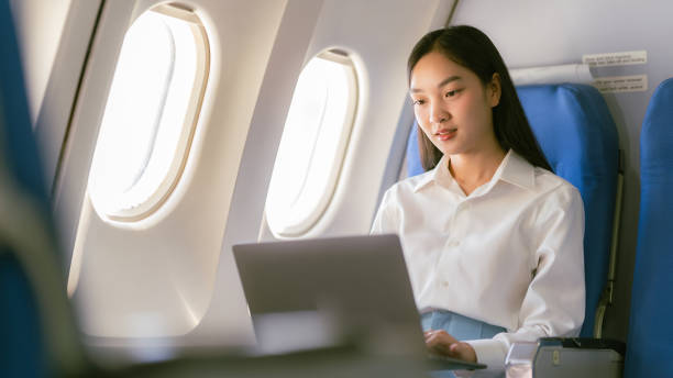 istock Young Asian woman using laptop, internet, working online, sitting near window in first class on airplane during flight, travel and business concept 2155712954