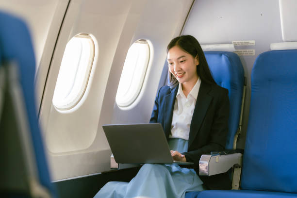 istock Young Asian woman using laptop, internet, working online, sitting near window in first class on airplane during flight, travel and business concept 2155713128