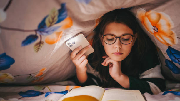 Girl reading a book under blanket lights with lantern from her phone