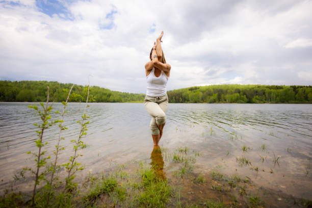 A female yoga instructor performs a balancing pose in the lake water, the serene environment highlighting her focus and tranquility.