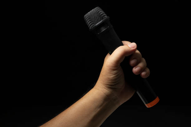 black microphone Male singer's hand holding microphone on modern singing stage On a black background and hands