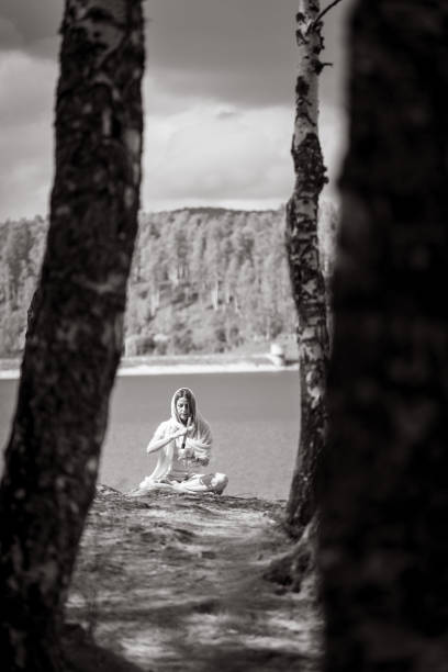 With a scarf draped around her, a spiritual woman sits beside the water, practicing music meditation.