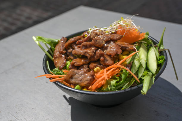 istock Asian teriyaki dish with marinated beef, vegetables and salad in a black bowl on a gray table, copy space, selected focus 2155739471