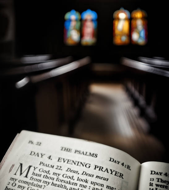 Color image depicting a close up wide angle view of the pages of an open bible on the altar of an Anglican church. Focus is on the bible in the foreground, while the background consists of the defocused interior of the church. Wooden pews recede into the distance and the lights illuminating the church appear as out of focus balls of light. The church has a warm, welcoming orange glow. Lots of room for copy space.