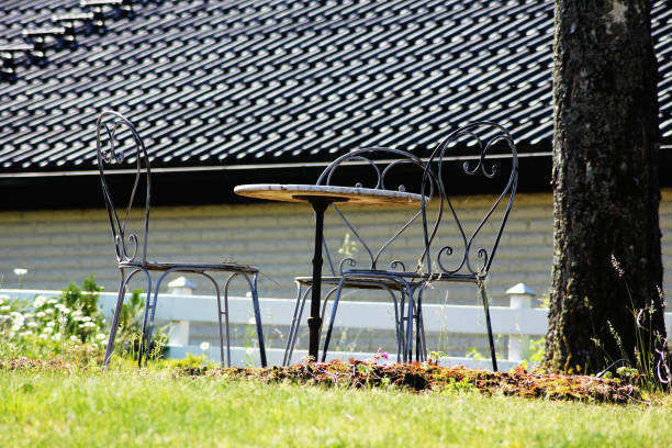 In a serene park during autumn, five white chairs lean against a rustic wooden table, surrounded by a blanket of colorful fallen leaves. The peaceful atmosphere invites relaxation.