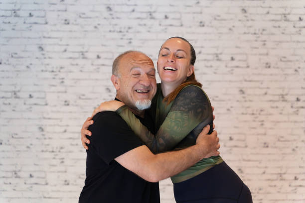 istock Laughing elderly man and young woman hugging joyfully against a white brick wall. 2155755131