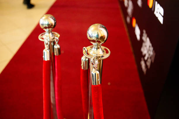 Unoccupied iconic runner between roped stanchions. Red carpet leading up short staircase. Lighting equipment arranged near walkway.