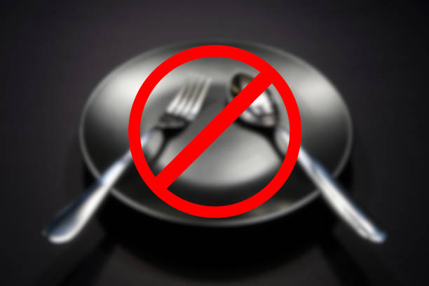 Silver cutlery set together placed over empty food plate with black background close up view with ban or alert sign blurry background focus on foreground