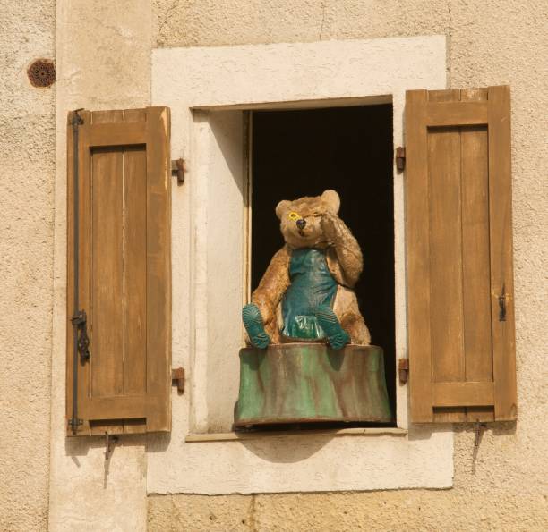 A carved Blowing Bubbles wood bear sits on a window sill with shutters