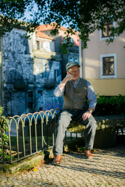 istock A middle-aged man pretends to make a phone call while sitting in a park, adding a playful touch to the peaceful setting. 2155765914