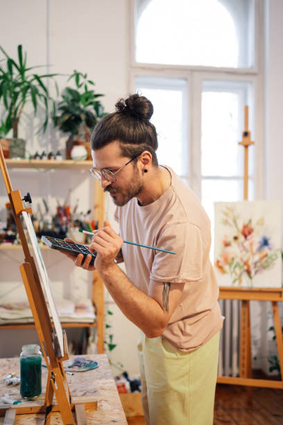 istock Creative tattooed artist is painting on easel at art studio. 2155775592