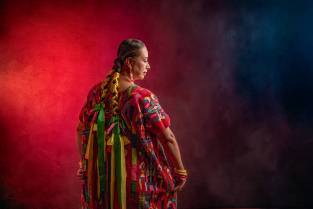 A woman wearing a red and green dress with a green ribbon tied around her waist Mexican Latin woman from Oaxaca Mexico, indigenous from the Guelaguetza A woman wearing a red and green dress with a green ribbon tied around her waist. She is standing in front of a red background elderberry photos stock pictures, royalty-free photos & images