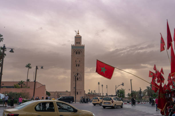 Koutoubia Mosque, Marrakech, Morocco - March 18, 2024: The majestic minaret towers over the cityscape at dusk, hoisted with the Moroccan flag.