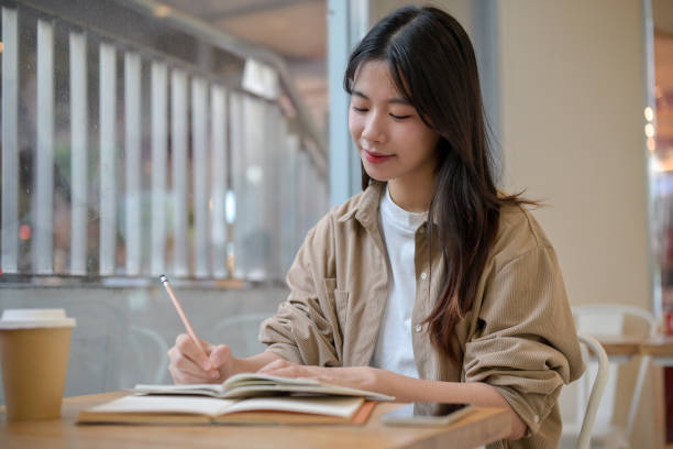 istock A young Asian female college student doing her homework at a cafe, writing something in a notebook. 2155791070