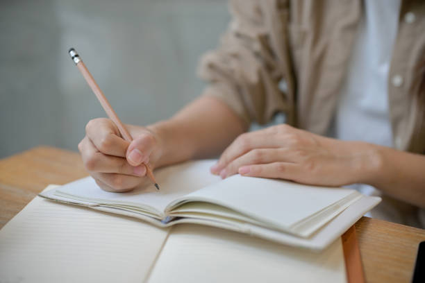 istock A female college student holding a pencil, writing something in a notebook at a table indoors. 2155791071