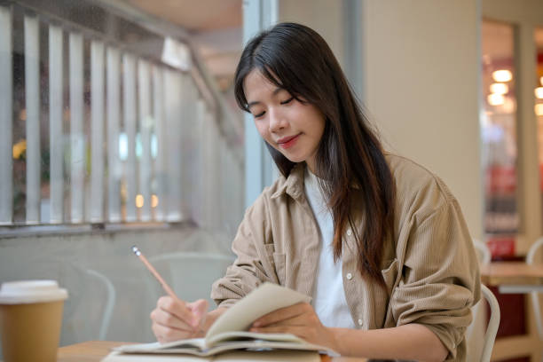 istock A young Asian female college student doing her homework at a cafe, writing something in a notebook. 2155791072
