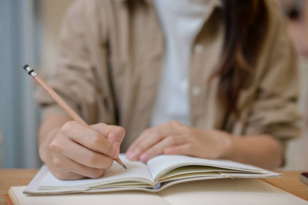istock A female college student holding a pencil, writing something in a notebook at a table indoors. 2155791073