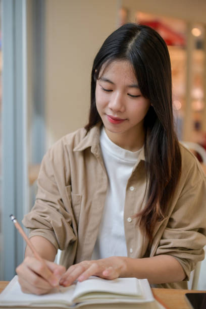 istock A young Asian female college student doing her homework at a cafe, writing something in a notebook. 2155791905