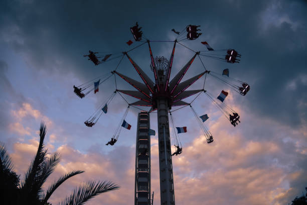 A swing ride at the Jardin des Tuileries in Paris during the evening. The ride is adorned with several French flags, and the sky is beautifully colored with hues of pink and blue from the setting sun.