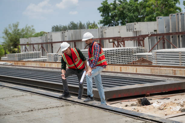 istock Engineer or architect with a hardhat examines the schedule on a set of plans. Two businessmen, both engineers, at the construction site. 2155800290