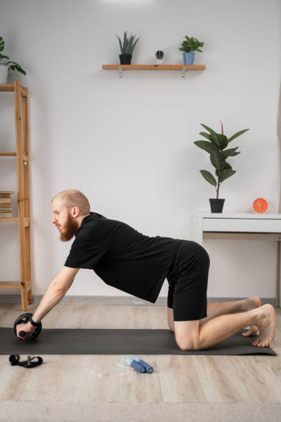 istock Handsome bearded man doing exercise with abs wheel on mat. Athletic man doing fitness workout at home. Bodybuilding, fitness workout concept 2155801235