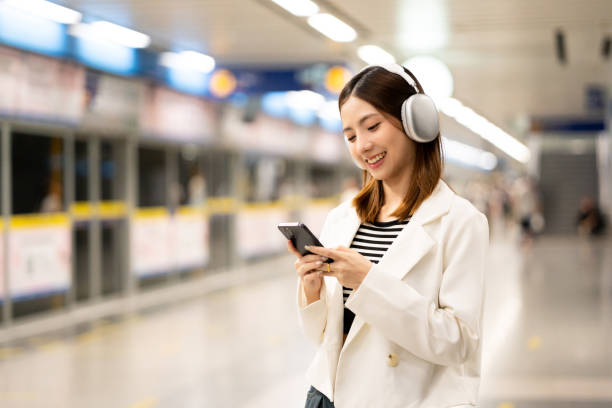 istock Young asian woman using smartphone application navigate location destination while travel by subway. Asian female with headphone listen to the music by cell phone while traveling in train transport 2155802153