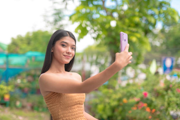 A young Thai woman poses for the camera while taking a different picture of herself on her cellphone.