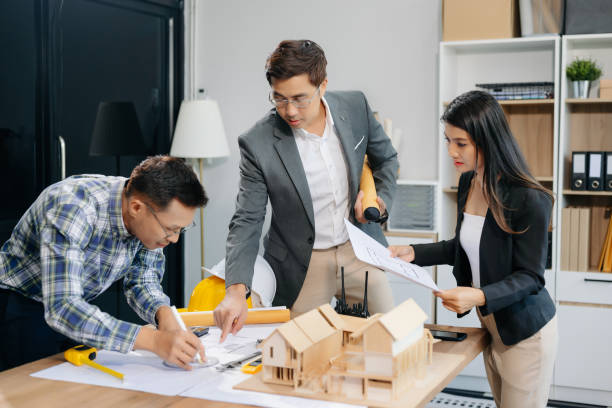 istock Engineer teams meeting working together wear worker helmets hardhat with on architectural project site and making model house. Asian industry professional team 2155802542