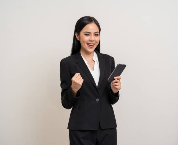 istock Attractive elegant young asian business woman using cellphone standing on isolated background. Happy Excited young asian female formal black suit holding smartphone contract service with customer 2155803608