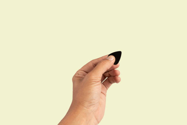 istock Black male hand holding a guitar pick isolated on light green background 2155805744