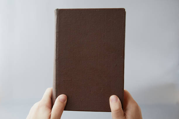 istock An old book with a brown cover without a title held by two hands, close-up. Old law, biblical truths 2155805838