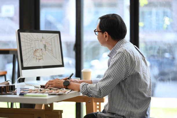 istock Side view of senior male in eyeglasses working with sketches interior design on computer monitor in office 2155806821