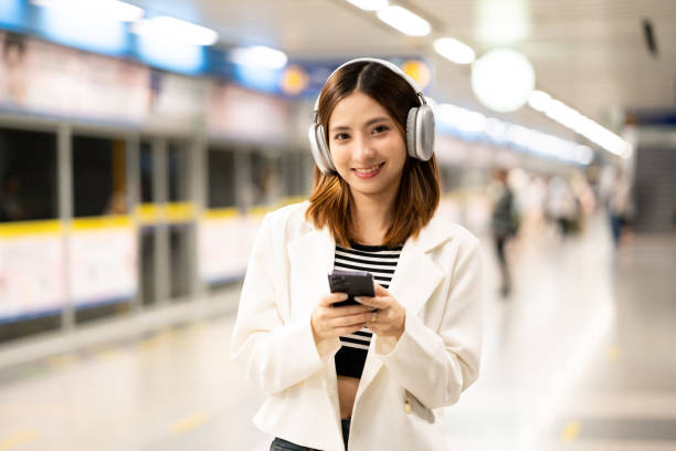istock Young asian woman using smartphone application navigate location destination while travel by subway. Asian female with headphone listen to the music by cell phone while traveling in train transport 2155807304