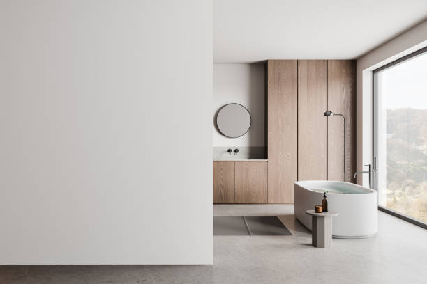 istock Minimalist bathroom with a bathtub, large window, wooden cabinets, and a blank wall. Light background. Interior design concept. 3D Rendering. 2155808859